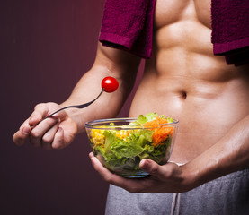 Muscular man holding a bowl of salad on grunge background