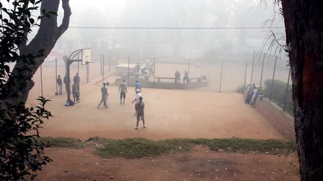 Foggy view of young men playing basketball on a dirt court.