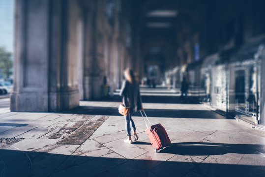 Tilt shift photo of a young girl with red luggage exit from Mila