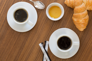 Two cups of coffee with croissants, honey and sachets sugar on  wooden table. top view