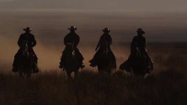  Four western cowboys riding horses at dusk ride past camera, slow motion pan