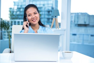 Smiling businesswoman on phone using laptop