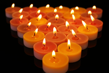 Many burning small candles on dark background, close-up