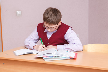 boy with glasses sitting at a desk writing