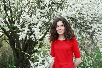 Naklejka premium Smiling beautiful young lady wearing red three quarter sleeve dress enjoying spring blooming fruit orchard