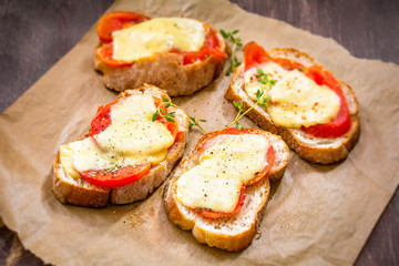 Crostini with tomato, cheese and thyme on parchment paper. Party appetizer or a snack. Selective focus