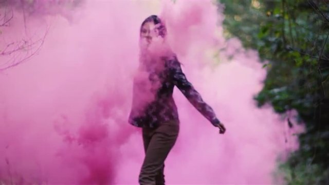 Beautiful girl in a forest spins around while holding a pink smoke grenade, slow motion