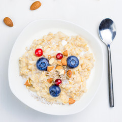Oatmeal porridge with berries, chia seeds and almonds in bowl on white background, top view, square composition