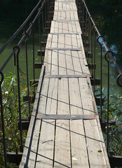 Old wooden footbridge hanged across a small river