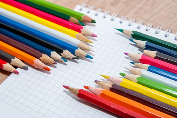 Set of colorful pencils lying in row on white paper sheet