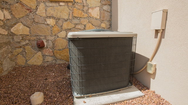 AC Unit Rise and Lower on Stones. camera rises and descends on an air conditioning unit in an arid location. Placed on a stones against a stone and stucco facade
