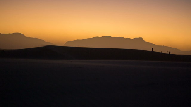 Windy Desert During Sunset with People Silhouettes. a shot of a desert during sunset with a lot of wind off the dunes and people in the distance
