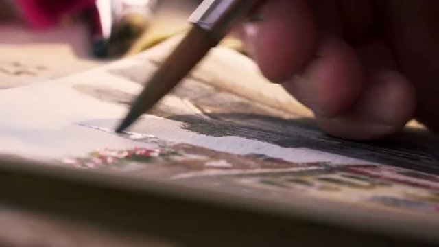 Shot of an artist painting in details in a watercolor painting.