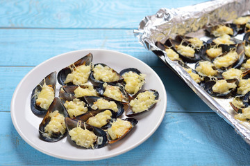 Plate with baked mussels with cheese and onions on a blue wooden