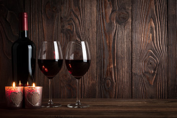 Red wine bottle, two glasses of wine and candles on the dark woo