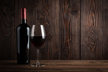 Red wine bottle and glass of wine on the dark wooden background