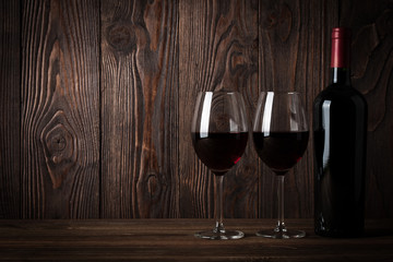 Red wine bottle and two glasses of wine on the dark wooden backg