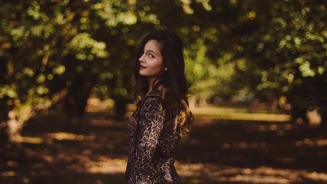 Beautiful girl in a dress spinning around and smiling in an orchard, in slow motion with bokeh