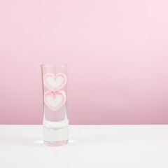 The lovely pink heart marshmallows in small narrow glass on white table.
