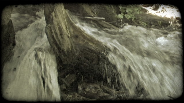 Water rushes past log in stream. Vintage stylized video clip.