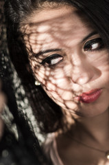 Headshot brunette model using patterned shadows as artistic effect on face while posing