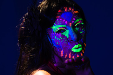 Headshot woman wearing awesome glow in dark facial paint, blue based with other neon colors and obscure abstract background, facing camera