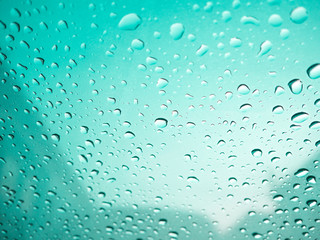 Raindrops on car's glass with blurry cloudy sky in village. Gree
