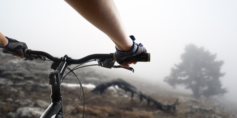 Hands in gloves holding handlebar of a bicycle. Mountain Bike cyclist riding single track. Healthy lifestyle active athlete doing sport