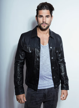 handsome young man posing on grey background with black leather jacket
