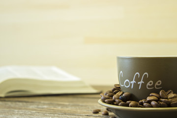 A cup of coffee with beans on the background of a  book. Focus on the edge of the cup