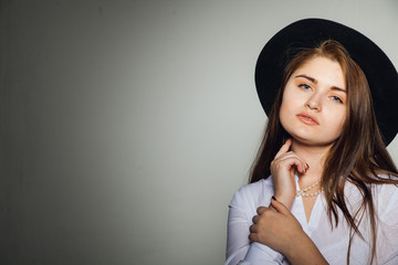 Awesome Caucasian attractive shy sexy female model with brunette hair posing on table in studio, wearing formal suit and hat, isolated on white background