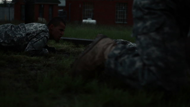 Two rows of soldiers crawling under low barbed wire at an obstacle course.