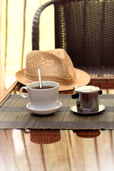 Morning coffee served in vietnam coffee filter on rattan table with a hat on table