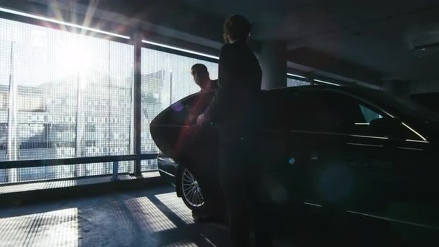 Driver opens the door for a businessman who speaks on the phone to step out of the black executive car at a garage parking. Shot on RED Cinema Camera.
