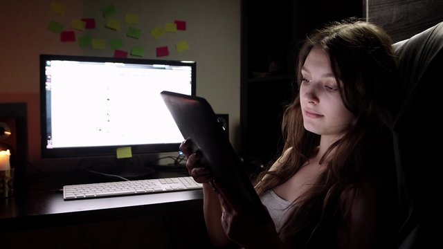 Teenage girl watching movie on tablet in bed at night