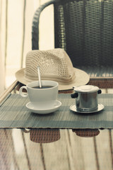 Morning coffee served in vietnam coffee filter on rattan table with a hat on table