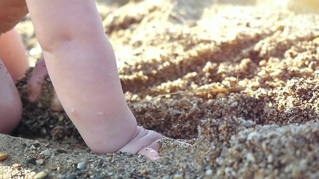 young baby playing in the sand and waves on the beach in slowmotion on sunny day