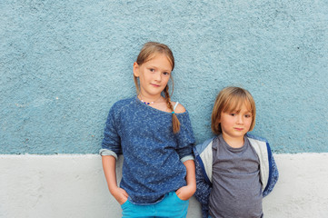 Fototapeta na wymiar Two kids, girl and little boy, posing outdoors, standing against blue wall, toned image