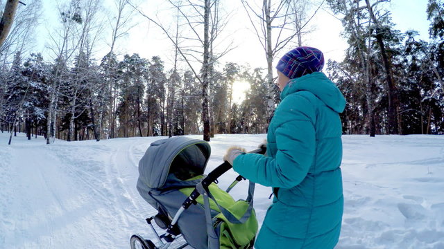 The girl with the baby in a carriage on walk in winter wood. 