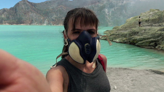 Woman in gas mask taking selfie photo, video by Ijen volcano in Java, Indonesia
