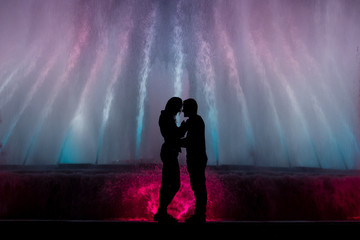silhouette of two lovers with colorful fountain background.