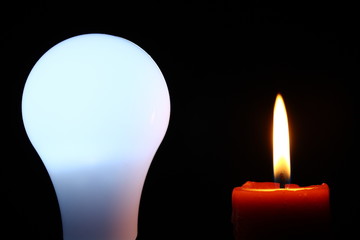 Electric bulb standing near a candle, being the oldest manufactured source of illumination.