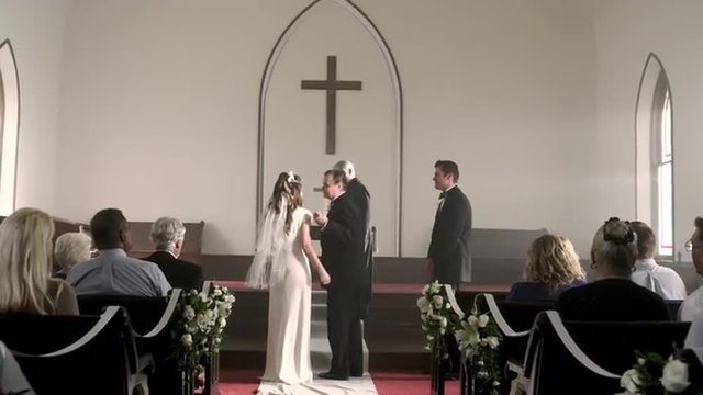 Father escorting bride to the groom at the front of a chapel.