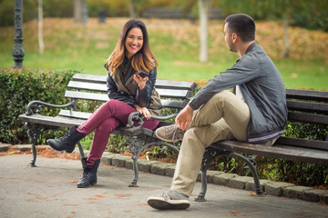 Two young people sitting on benches in a park and talking - obrazy, fototapety, plakaty
