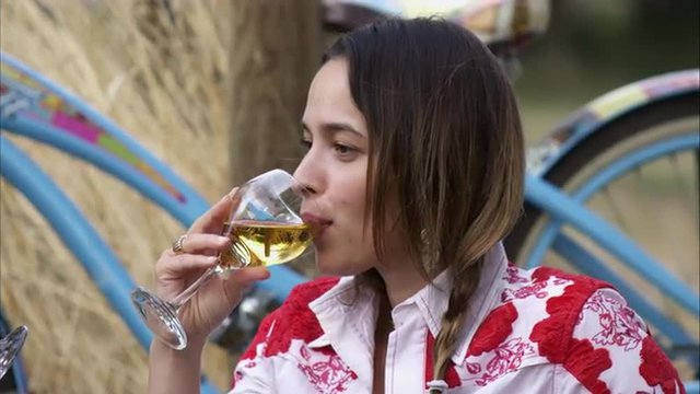 Slow handheld close-up shot of a young woman enjoying white wine at an outdoor picnic
