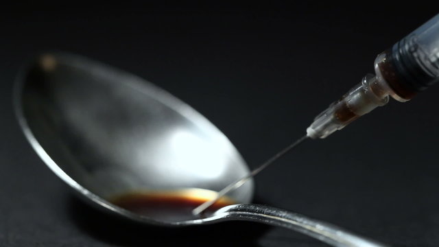 With spoon in gaining a syringe of the drug dose. Black background. Close-up