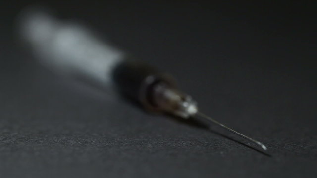 A syringe with a dose of a drug lies on a black table. Close-up. Dynamic change of focus