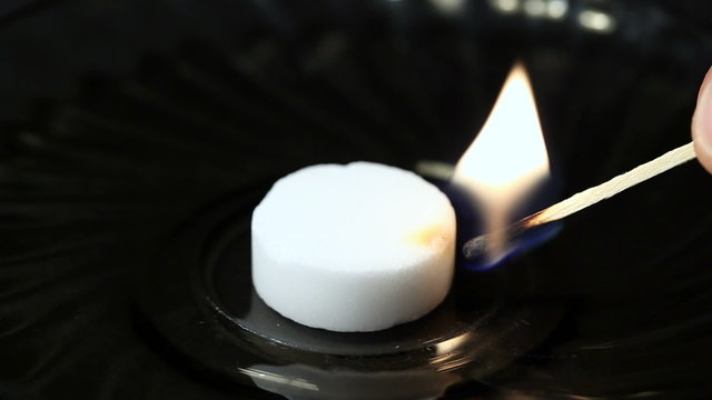 The match ignited fuel in the saucer tablet. Black background. Close-up