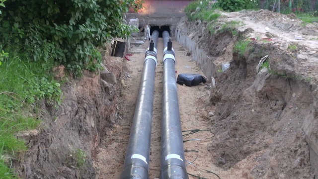 Central heating plastic black pipes in the ditch going into the house