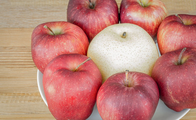 Group of red apple in white dish with chinese pear on wooden background